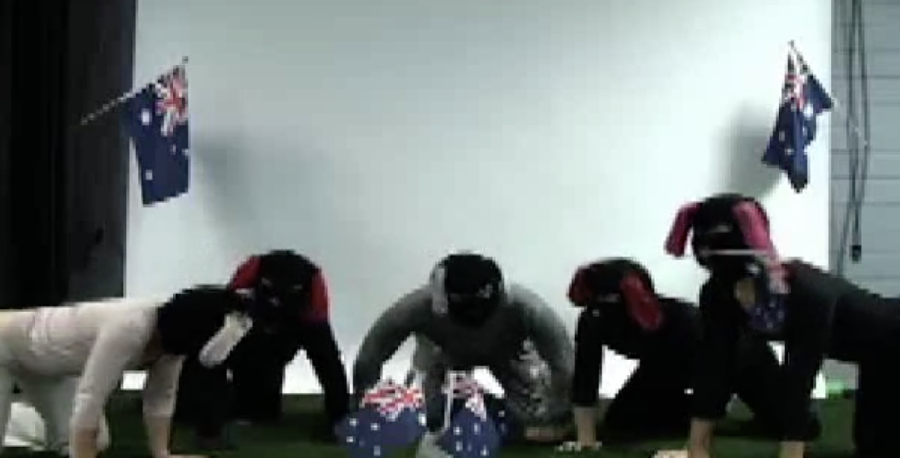 five people dressed as dogs on all fours surrounded by four small Australian Flags